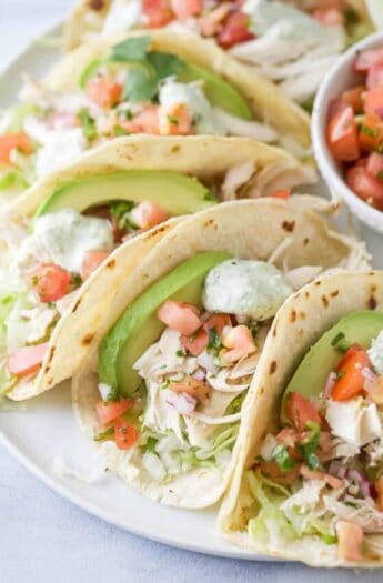 Rotisserie chicken tacos in warm corn tortillas, with avocado, cilantro-lime crema, and other toppings.