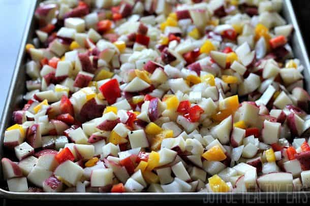 Diced bell peppers, onion, and red potatoes on a baking sheet