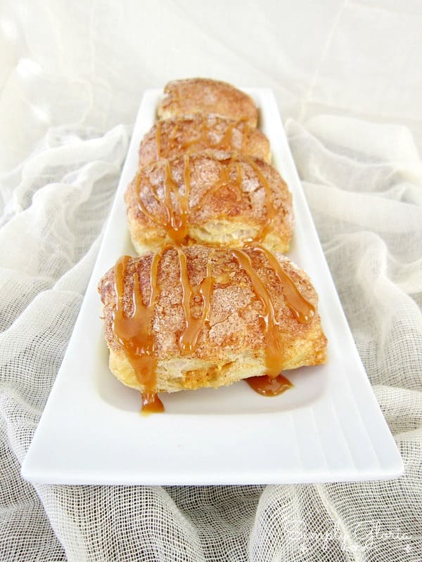 Side view of a line of pumpkin empanadas with caramel drizzle on a white rectangular plate