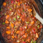 three bean chili in a crock pot with a wooden spoon