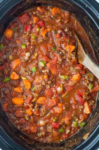 three bean chili in a crock pot with a wooden spoon