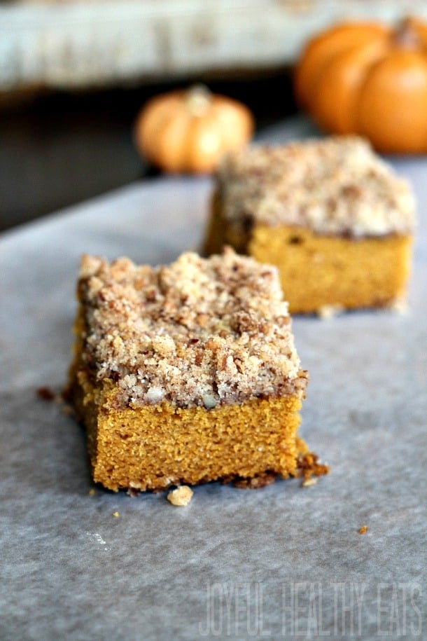 Two Pieces of Moist Pumpkin Spice Coffee Cake in Front of Two Mini Pumpkins