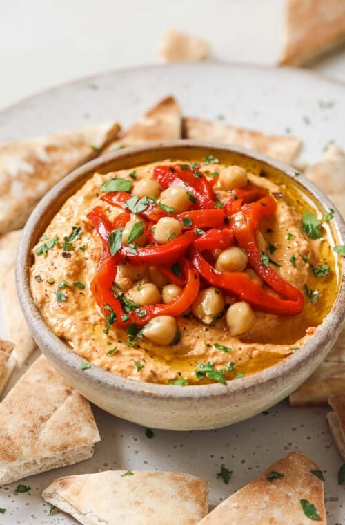 Bowl of hummus with roasted red peppers, chickpeas, and fresh parsley on top.