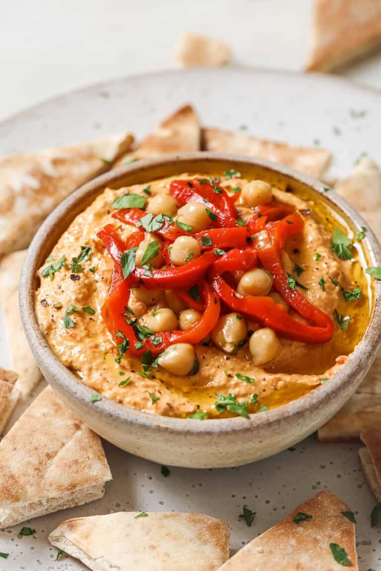 Bowl of hummus with roasted red peppers, chickpeas, and fresh parsley on top.