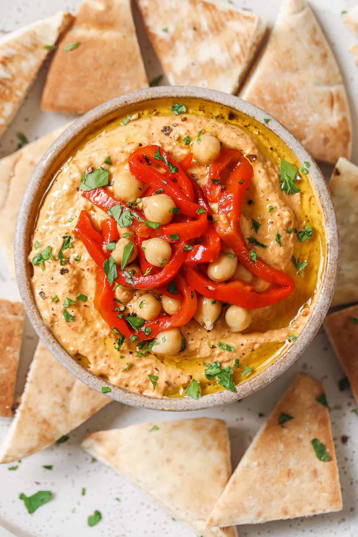 Bowl of roasted red pepper hummus with more chickpeas and peppers on top. 