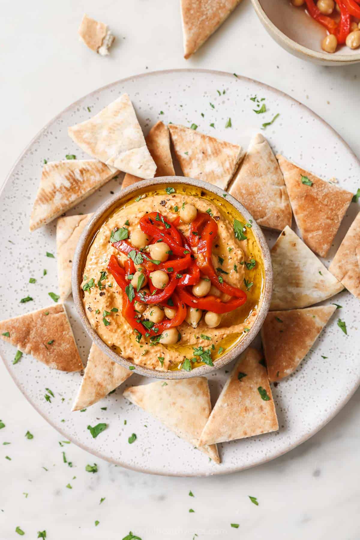 Creamy roasted red pepper hummus with crispy pita chips on the side. 