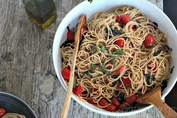 Spaghetti with burst grape tomatoes and basil in a serving bowl