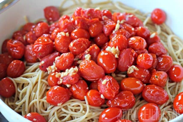 Burst tomatoes and garlic over spaghetti in a serving bowl