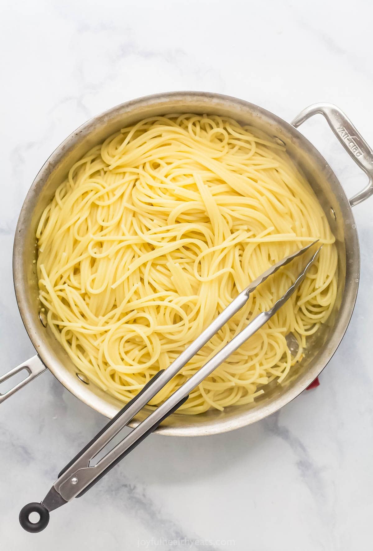 This Lemon Garlic Pasta is a 15-minute dinner elevated enough for a date night, but it's made with a short and simple list of ingredients! Spaghetti added to skillet with tongs