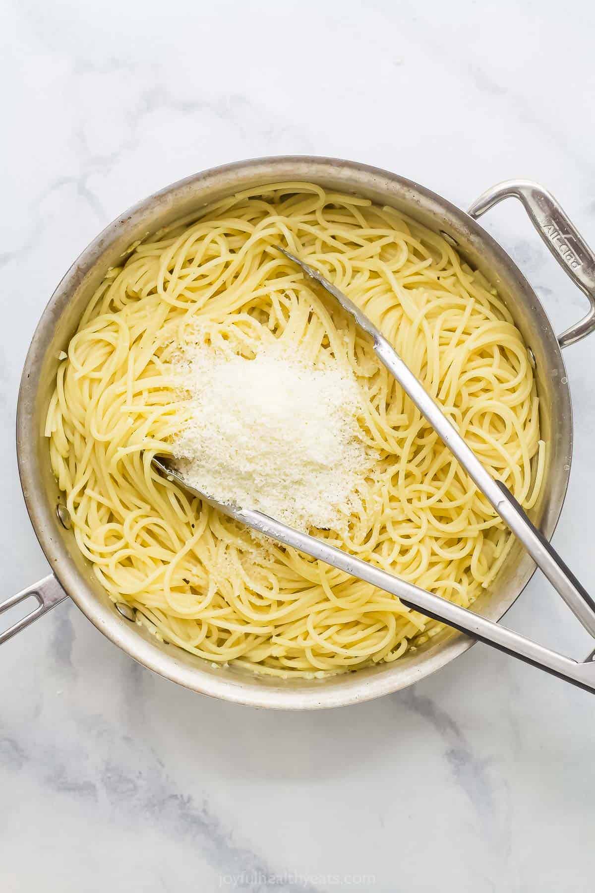 This Lemon Garlic Pasta is a 15-minute dinner elevated enough for a date night, but it's made with a short and simple list of ingredients! Tongs in pan of pasta with Parmesan on top