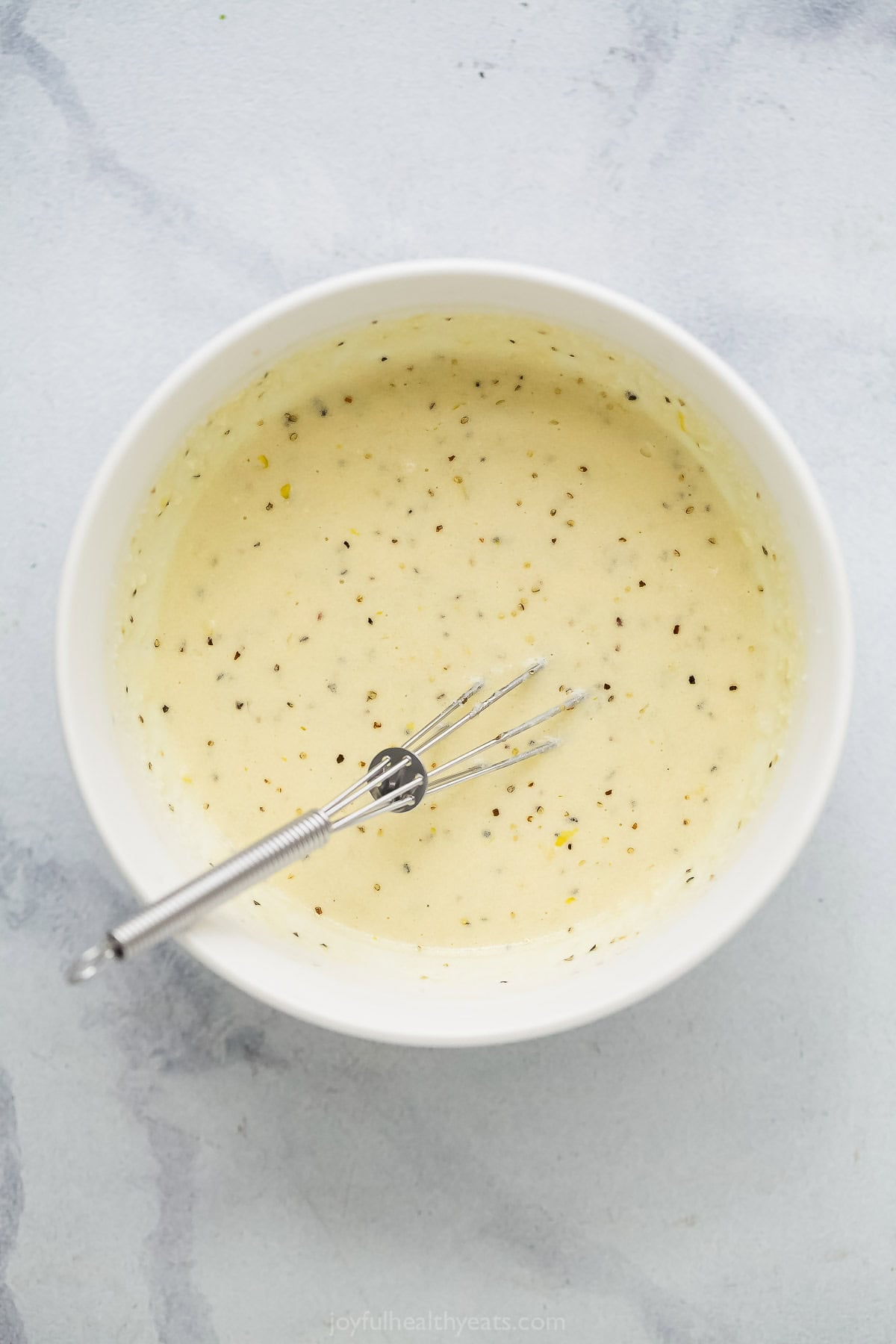 Bowl of homemade Caesar dressing with whisk.