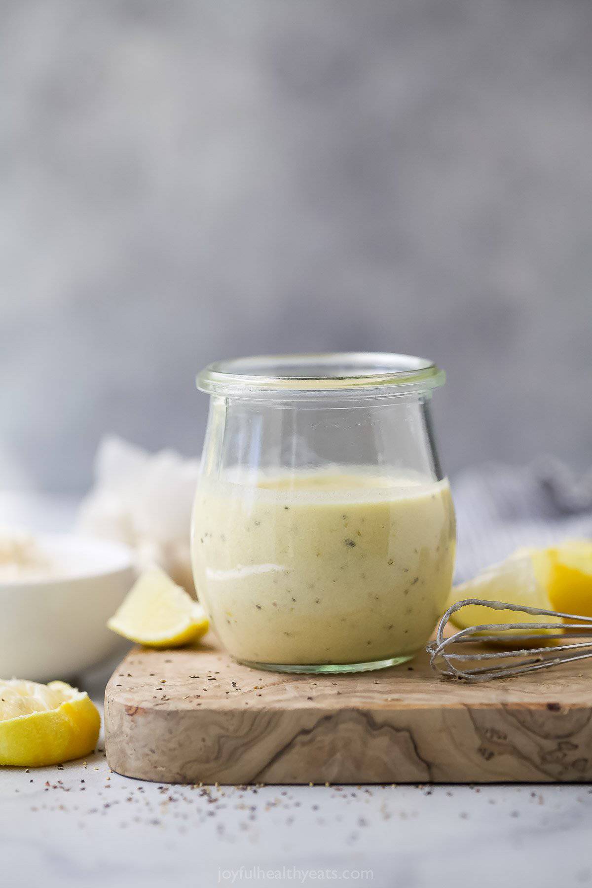 Jar of Caesar dressing on wooden board with fresh lemon wedges.