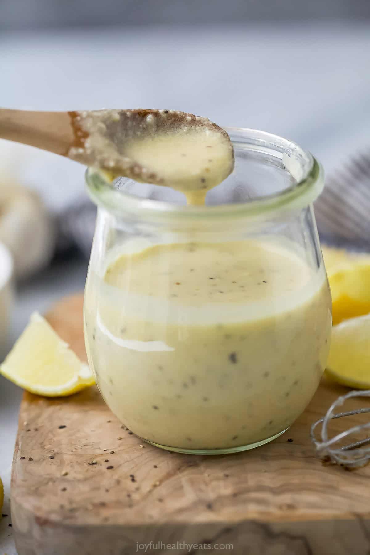 Spoon drizzling homemade Caesar dressing into jar.