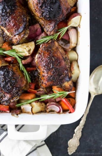 Angled photo of baked chicken with vegetables like onions, peppers, carrots, and potatoes in a baking dish.