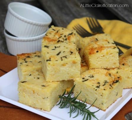 Squares of cornbread on a plate topped with rosemary and parmesan