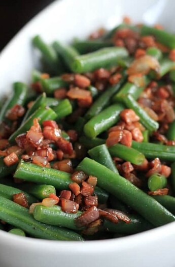 A bowl of green beans topped with pancetta and red onion