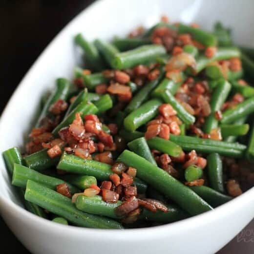 A bowl of green beans topped with pancetta and red onion