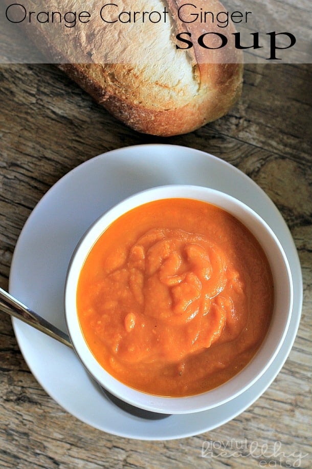 Orange Carrot Ginger Soup in a White Bowl Next to a Baguette