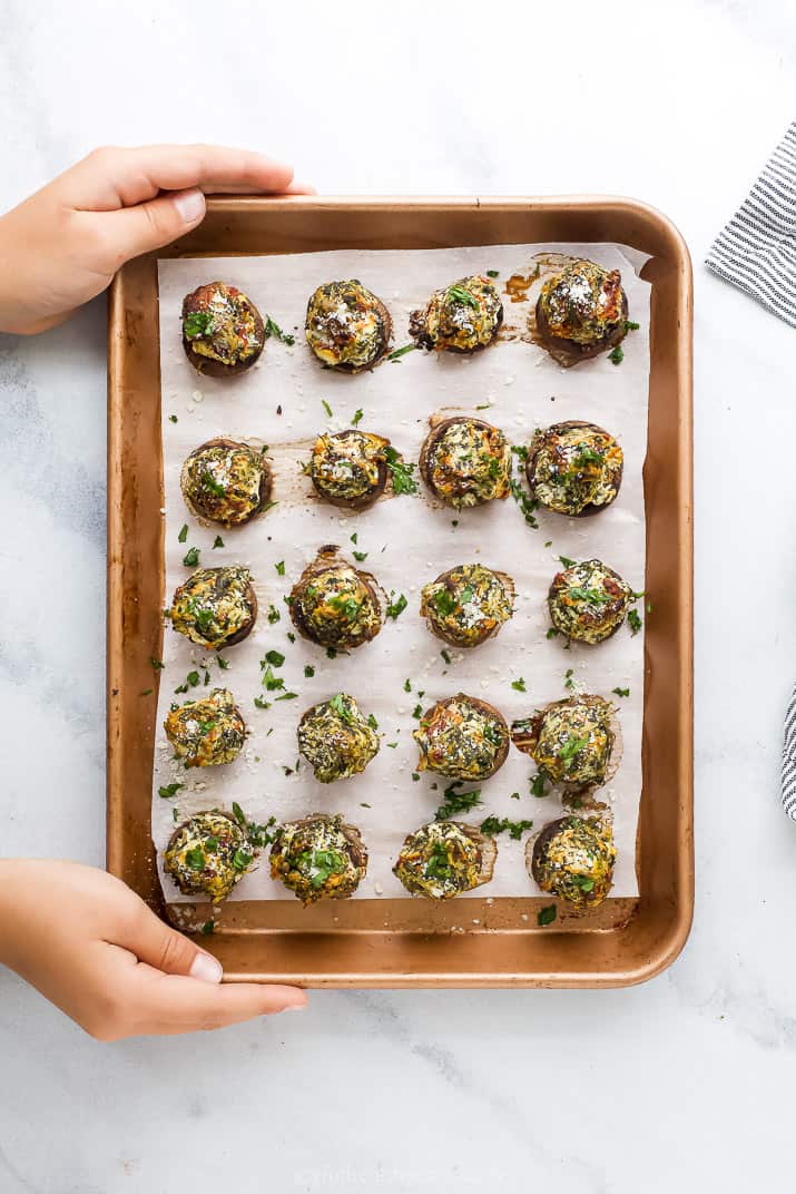 hands holding a baking sheet with stuffed mushrooms