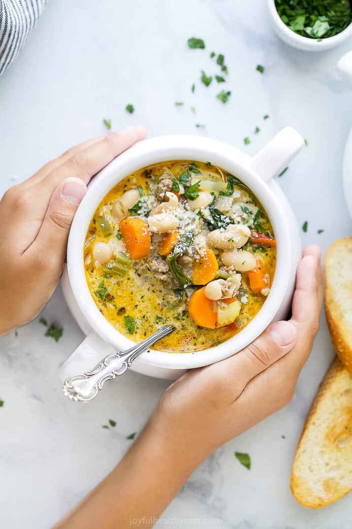 two hands holding a bowl filled with creamy tuscan white bean soup