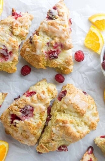 Four cranberry orange scones with cranberries and orange wedges on the side.