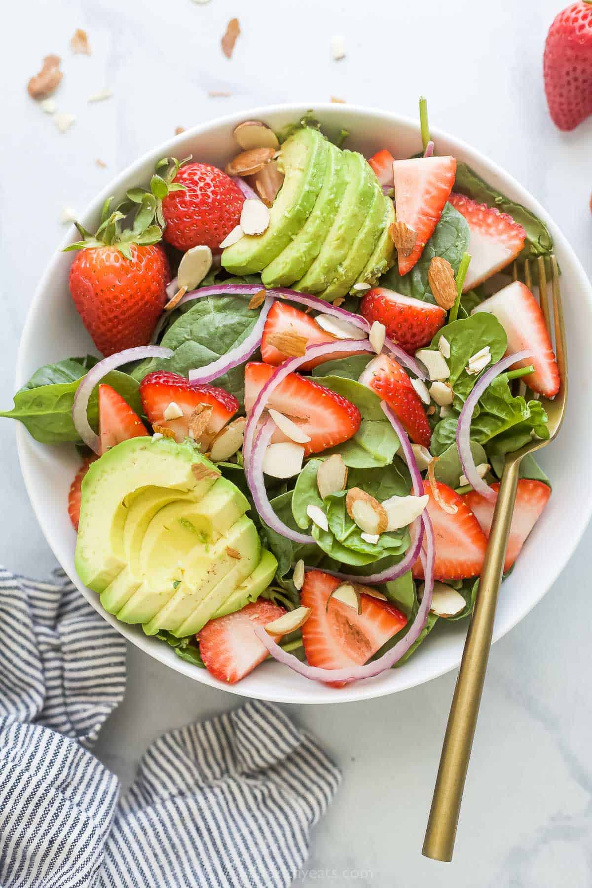 Bowl of spinach strawberry salad with avocado and red onion. 