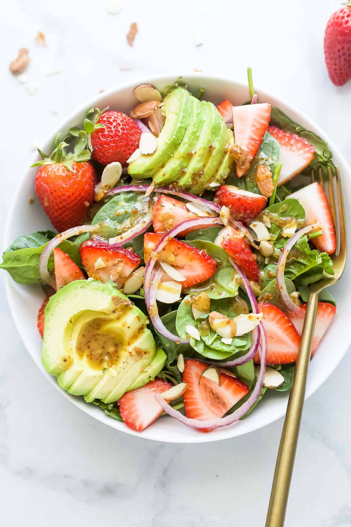 Close-up of a bowl of strawberry spinach salad with dressing. 