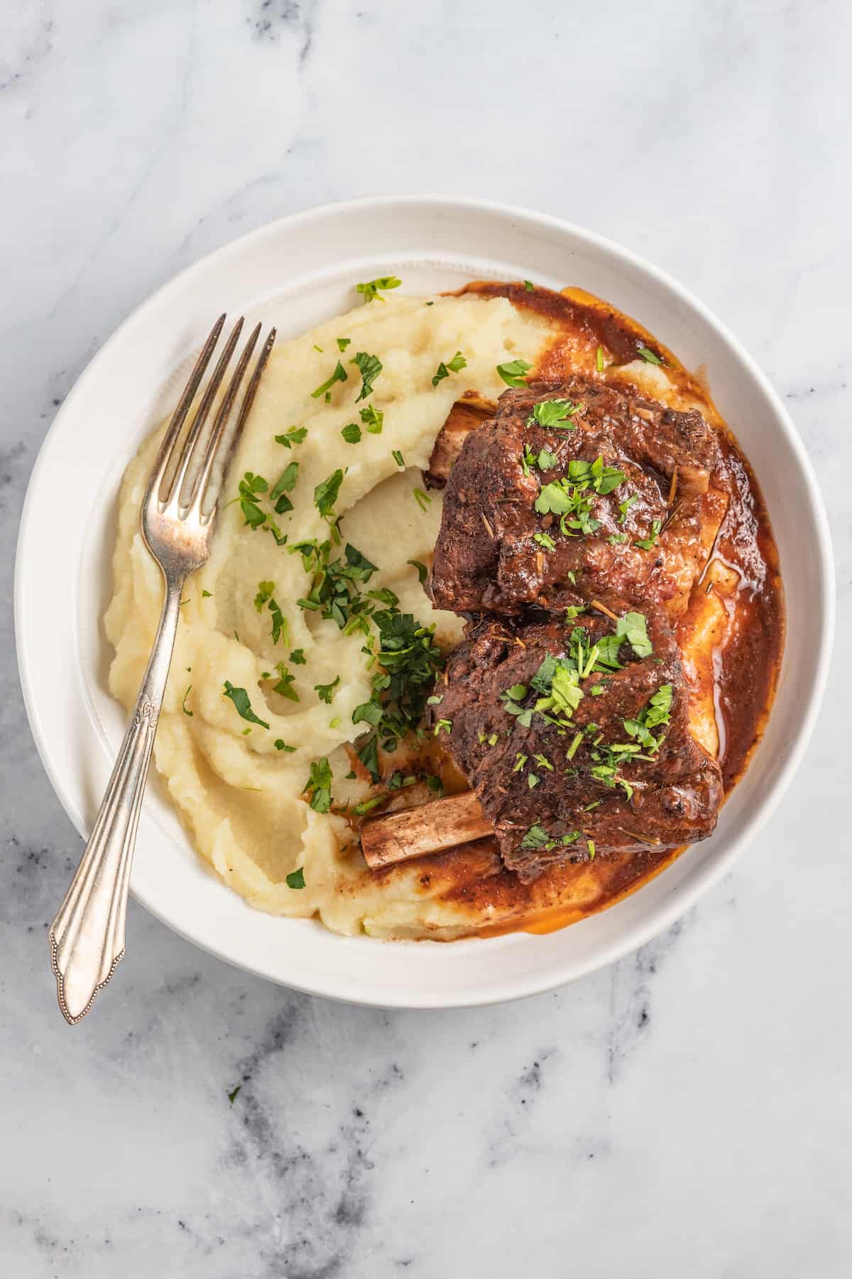 brasied balsamic short ribs plated with pureed potatoes and garnished with herbs