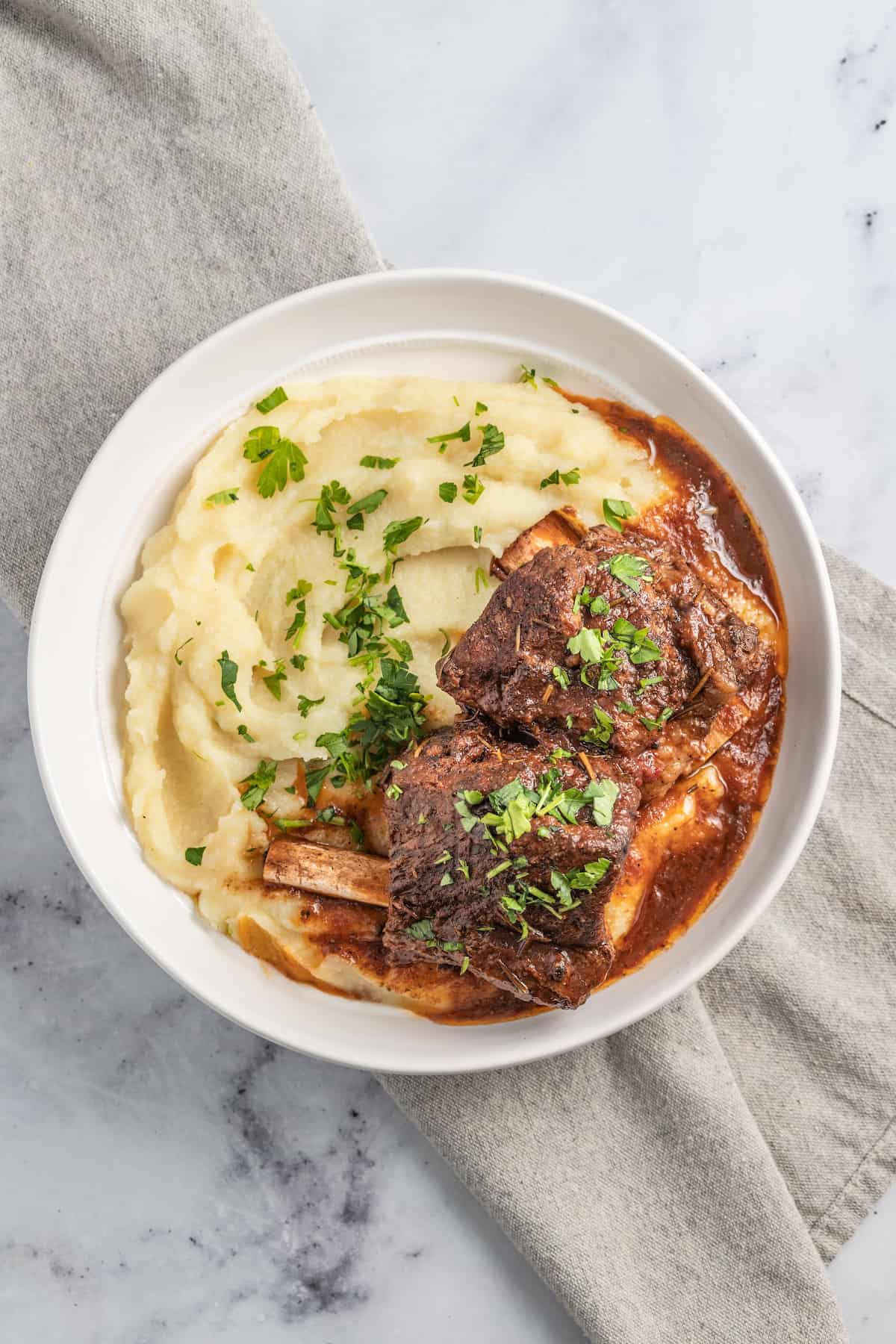 brasied balsamic short ribs plated with pureed potatoes and garnished with herbs