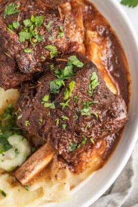 brasied balsamic short ribs plated with pureed potatoes and garnished with herbs