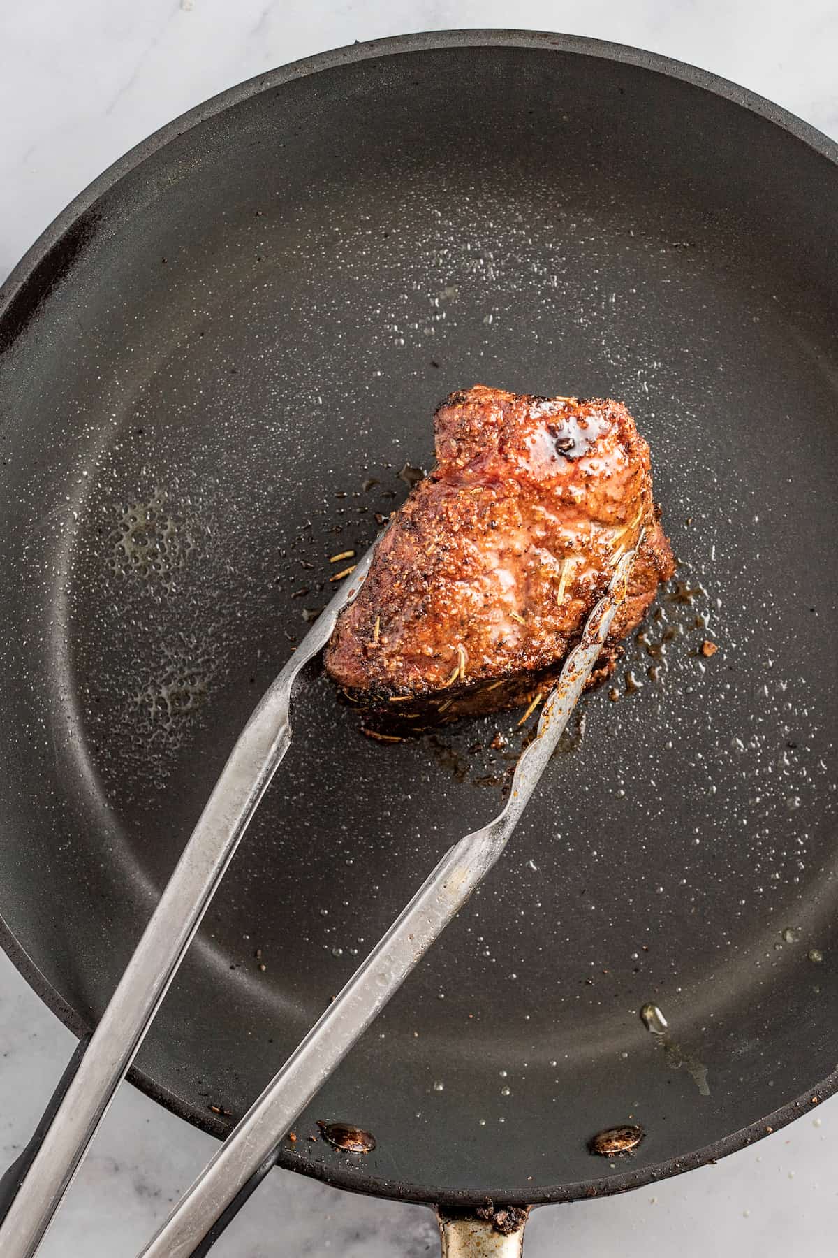 searing one short rib in a saute pan with tongs