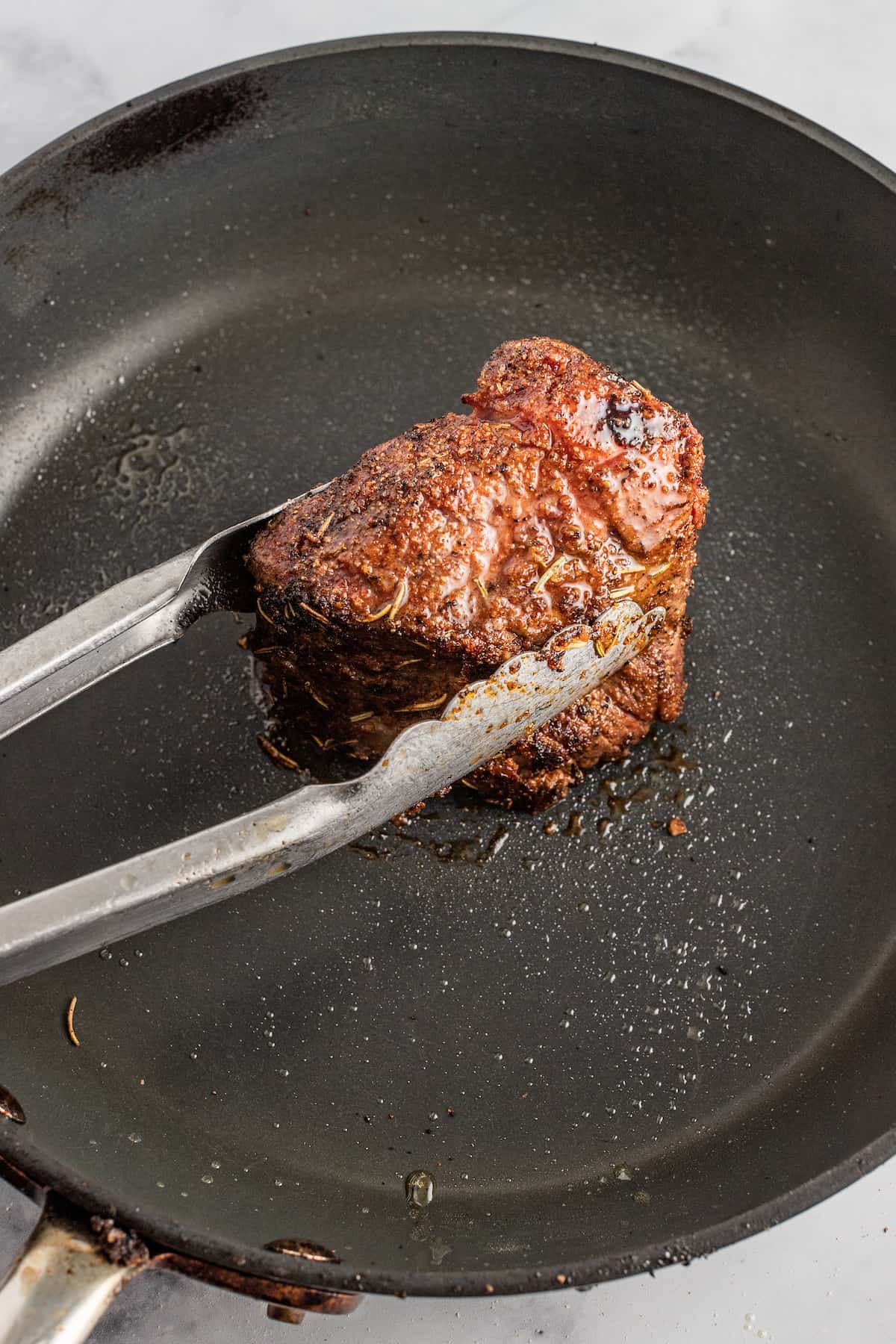 searing one short rib in a saute pan with tongs