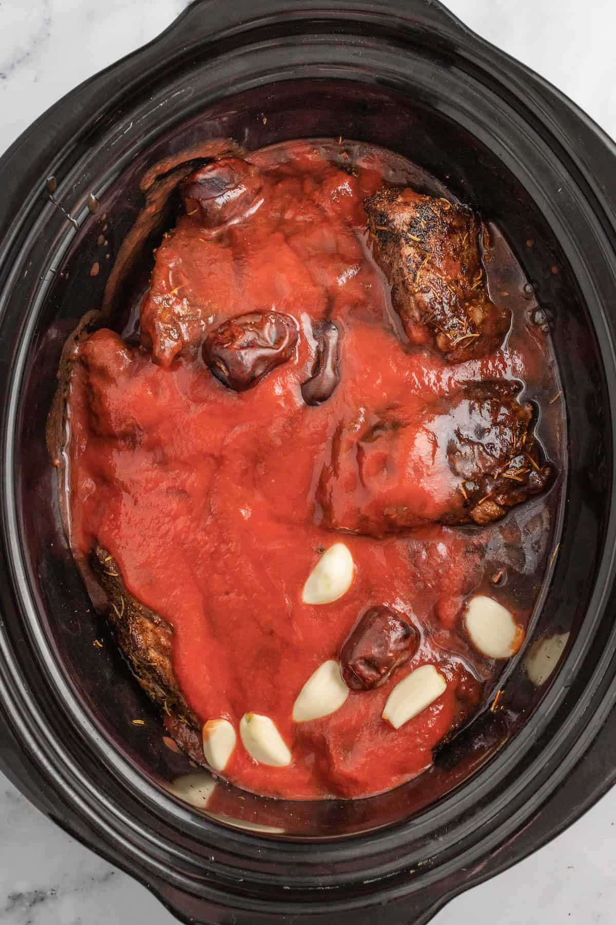 short ribs being smothered with tomato sauce and garlic in a slow cooker pot