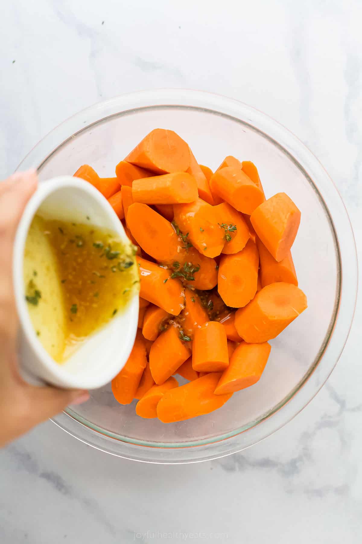 pouring an olive oil mixture over a bowl of cut up carrots