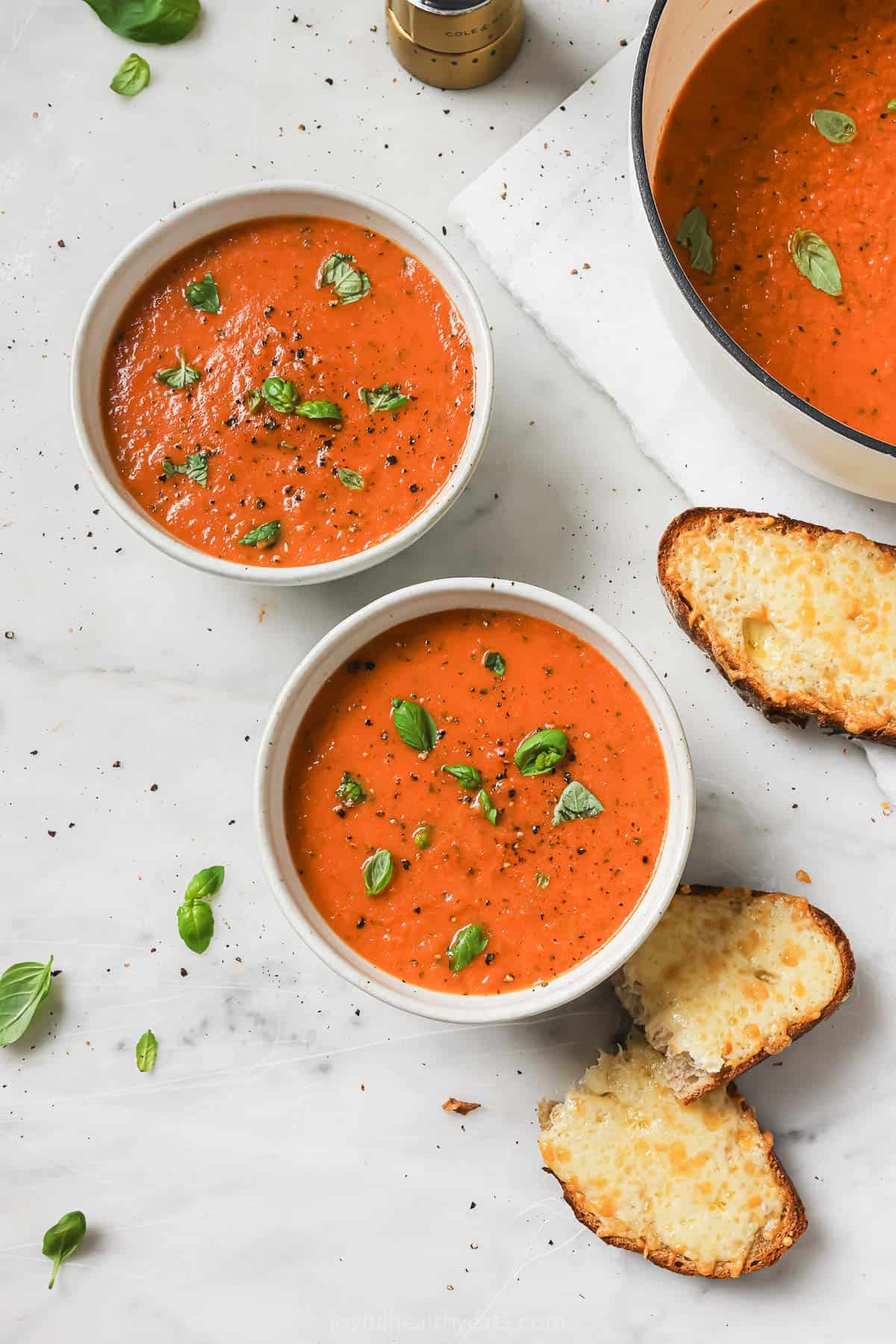 Two bowls of soup with sliced bread on the side. 