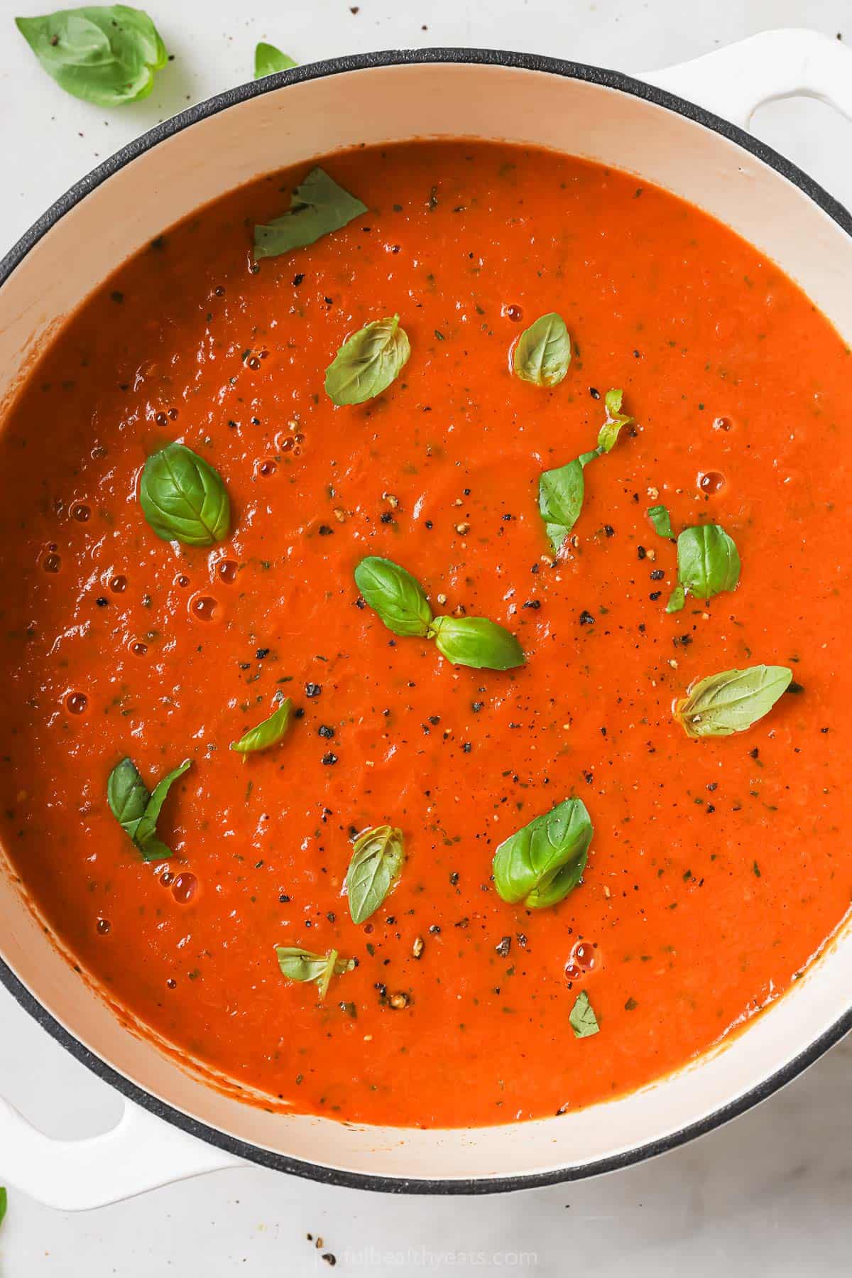 Pot of creamy tomato soup with basil.