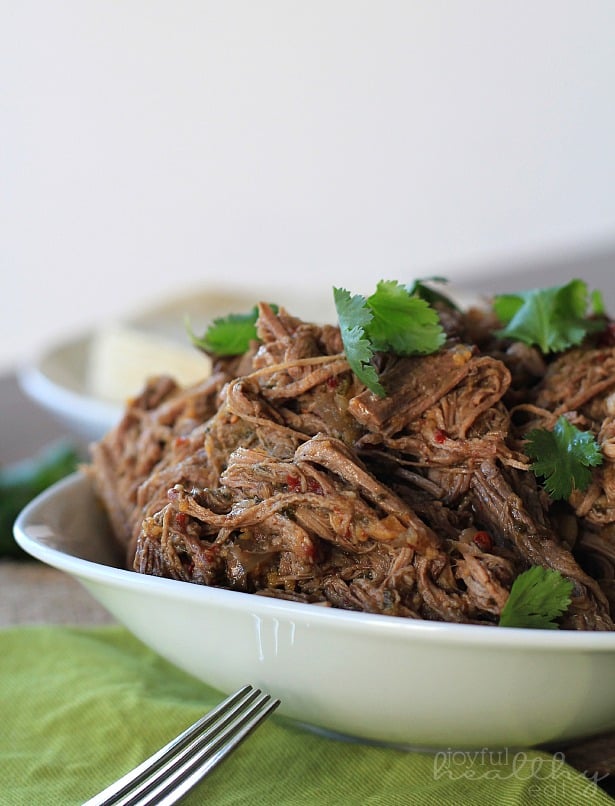 A close-up shot of Crock Pot chipotle beef barbacoa in a bowl with a fork in the foreground