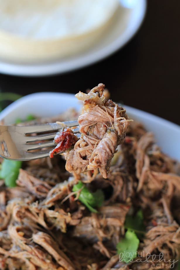 A fork holding a bite of shredded beef brisket over a plate piled with more shredded beef