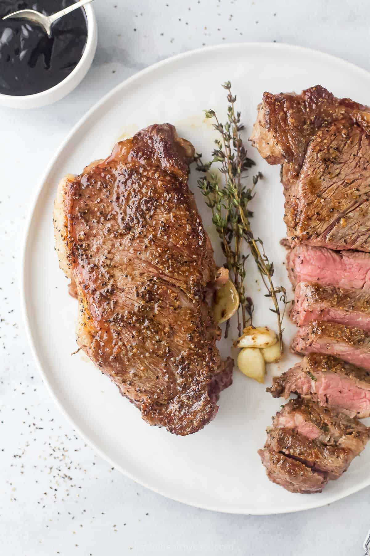 One whole New York strip steak and another one sliced on a plate. 