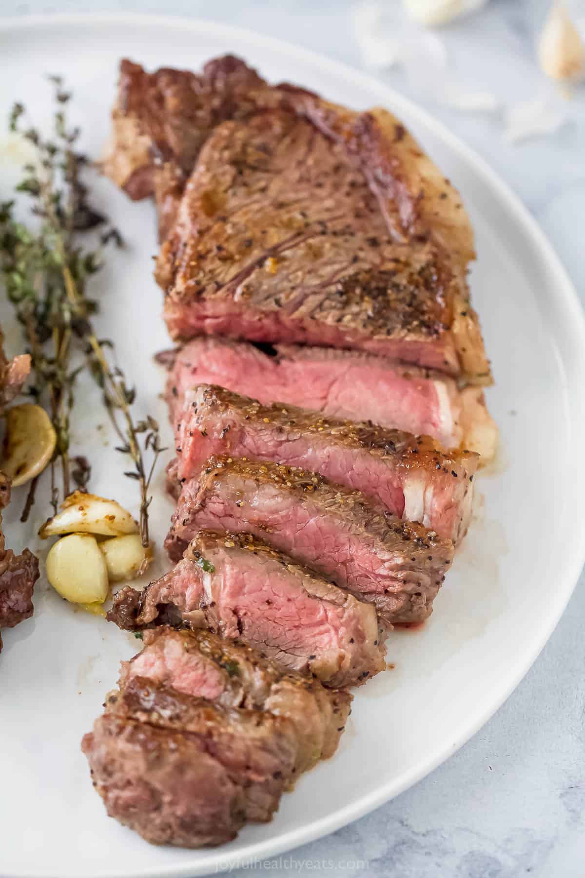 Sliced strip steak with thyme and garlic on a plate. 