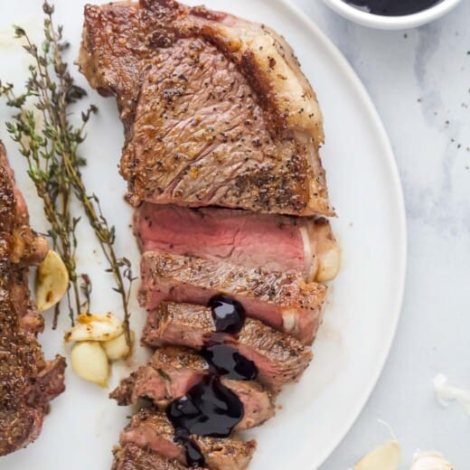 Sliced New York strip steak served on plate with balsamic reduction drizzled on top.