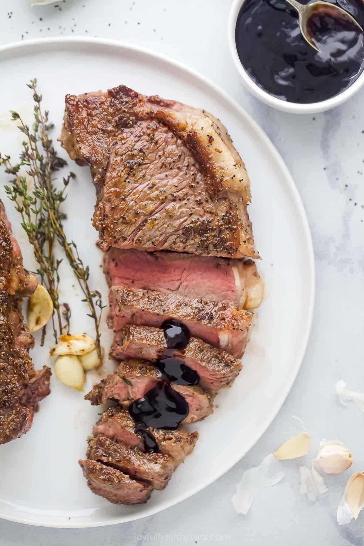 Sliced New York strip steak served on plate with balsamic reduction drizzled on top.