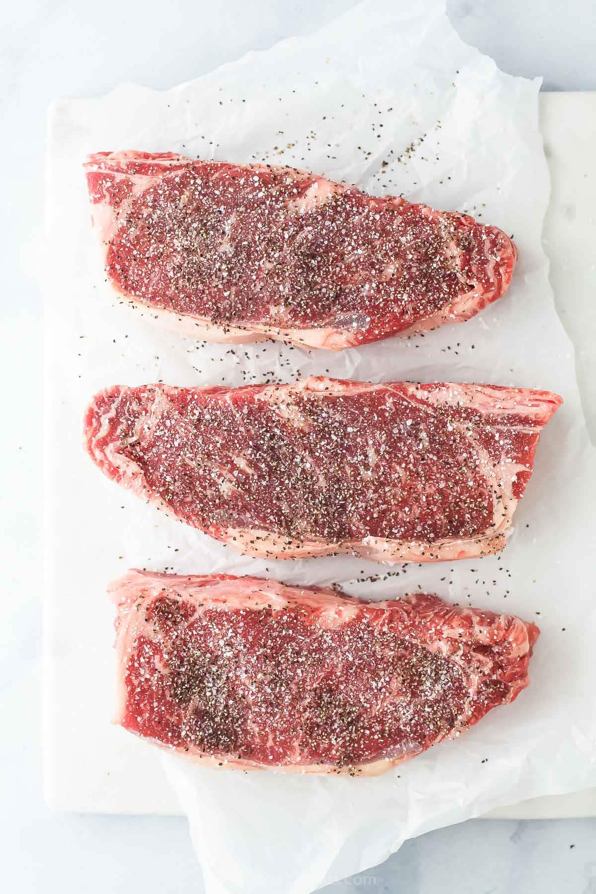 Raw steaks seasoned with salt and pepper.