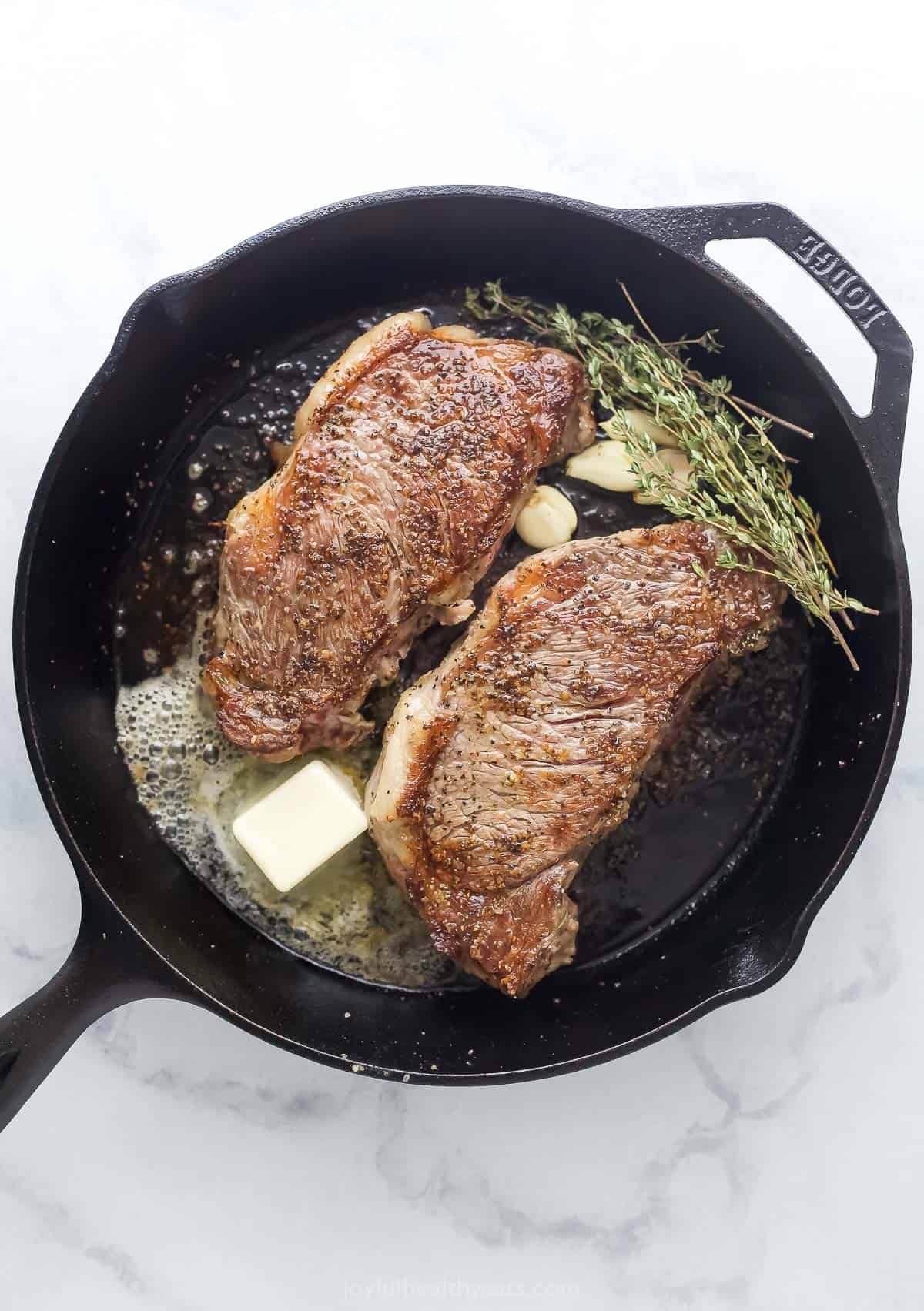 New Year strip steak in a large cast-iron skillet with butter, thyme, and garlic.