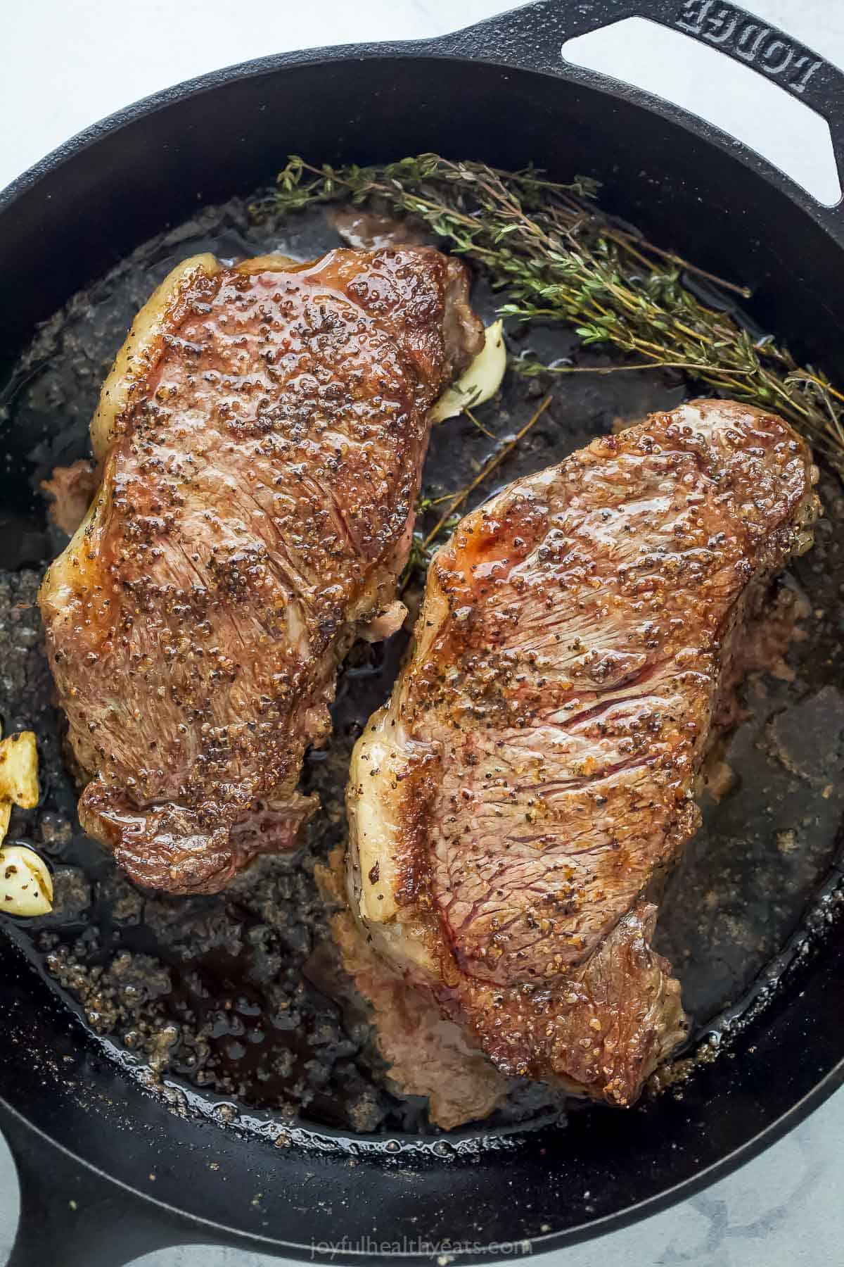 Steaks in the skillet with melted butter, garlic, and thyme.