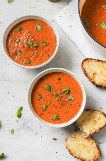 Two bowls of soup with sliced bread on the side.