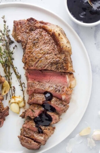 Sliced New York strip steak served on plate with balsamic reduction drizzled on top.