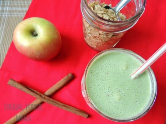 An Apple Ginger Crisp Smoothie Next to Two Cinnamon Sticks, an Apple and Granola