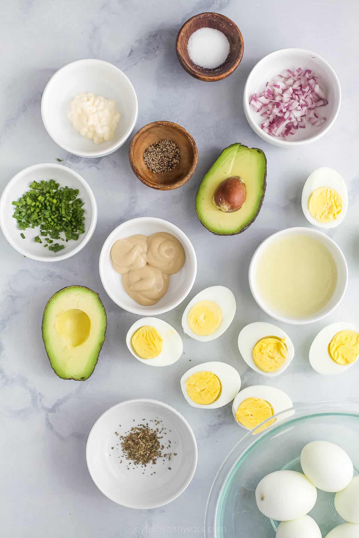 an assortment of ingredients to make avocado egg salad on a marble countertop