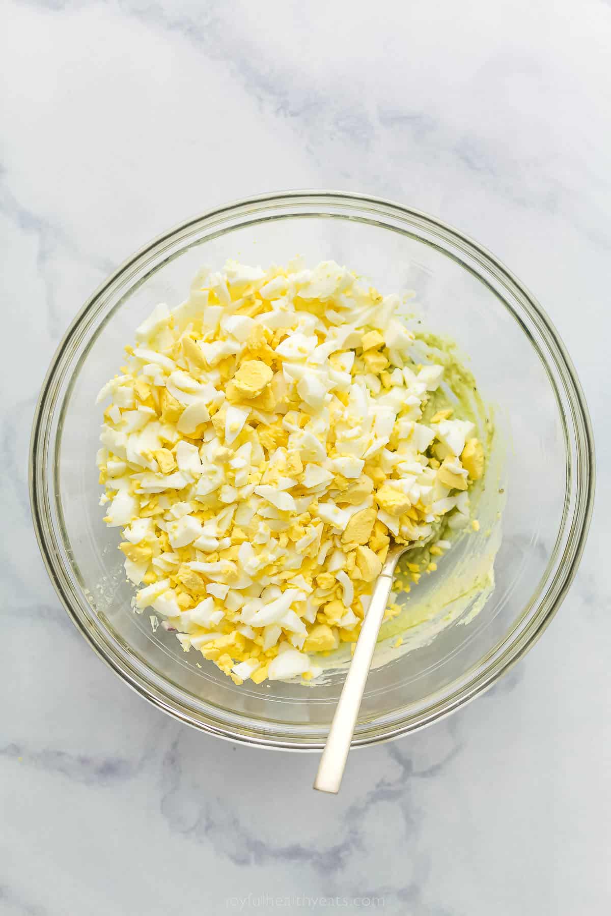 a glass bowl with crumbled eggs and creamed avocado underneath